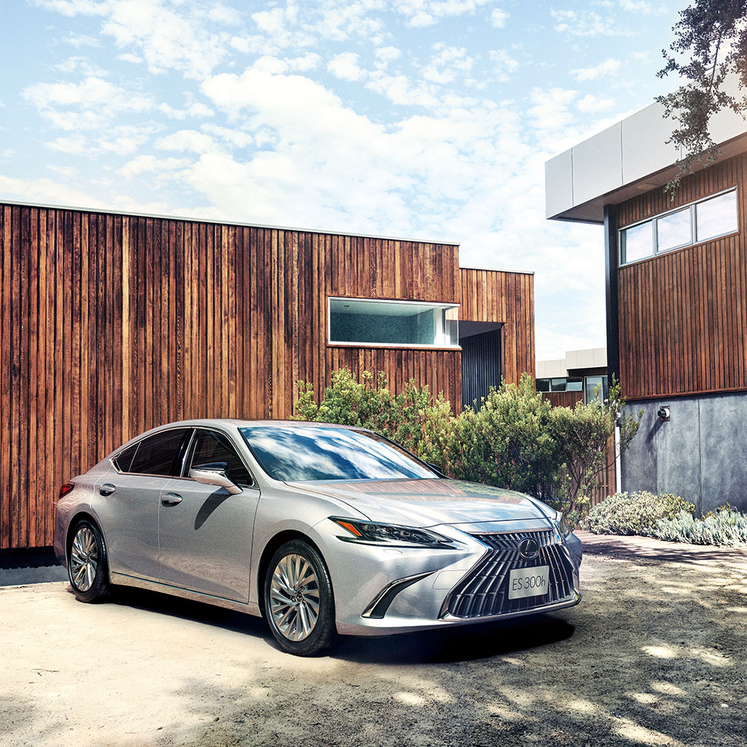 A silver ES Sedan parked next to a modern looking home.