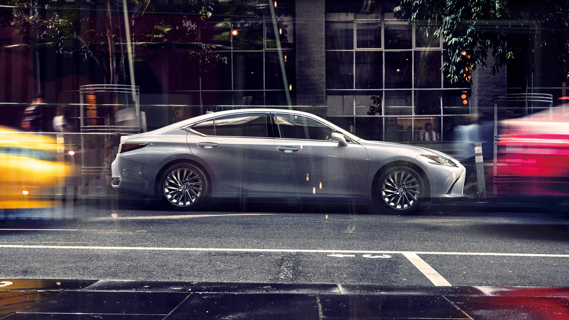 A grey coloured ES sedan parked on a tree lined city street in between a yellow car and a red car